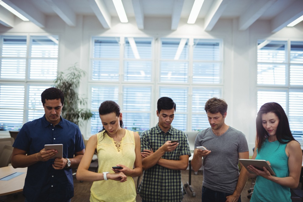 Three men and two women standing in an office with their phones showing digital tenant engagement