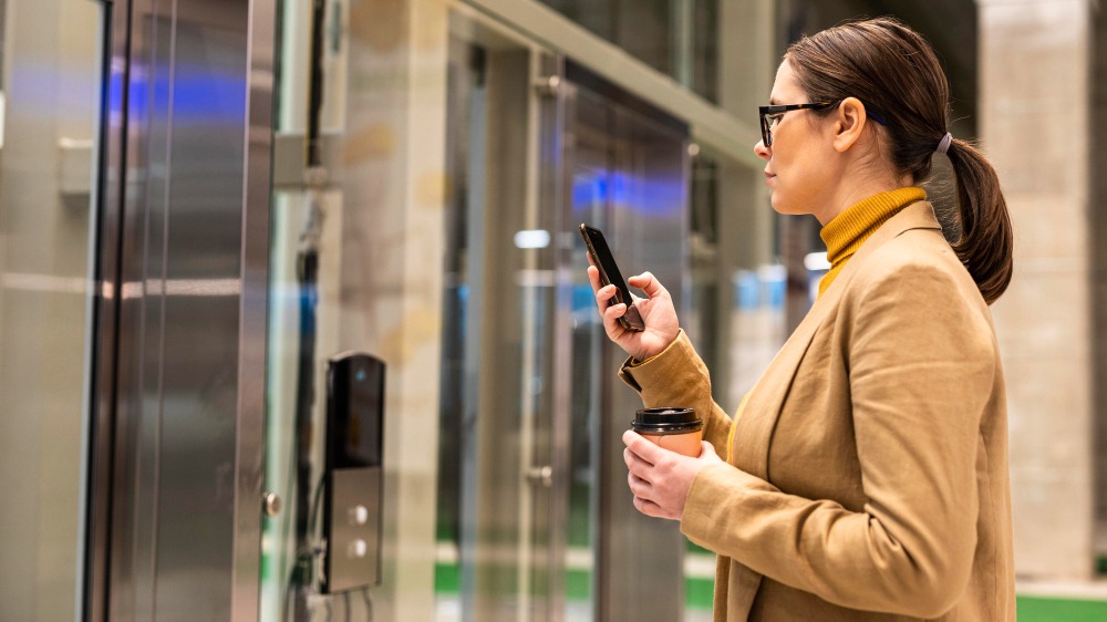 Woman holding a phone in front of a glass door to show IoT-based access control