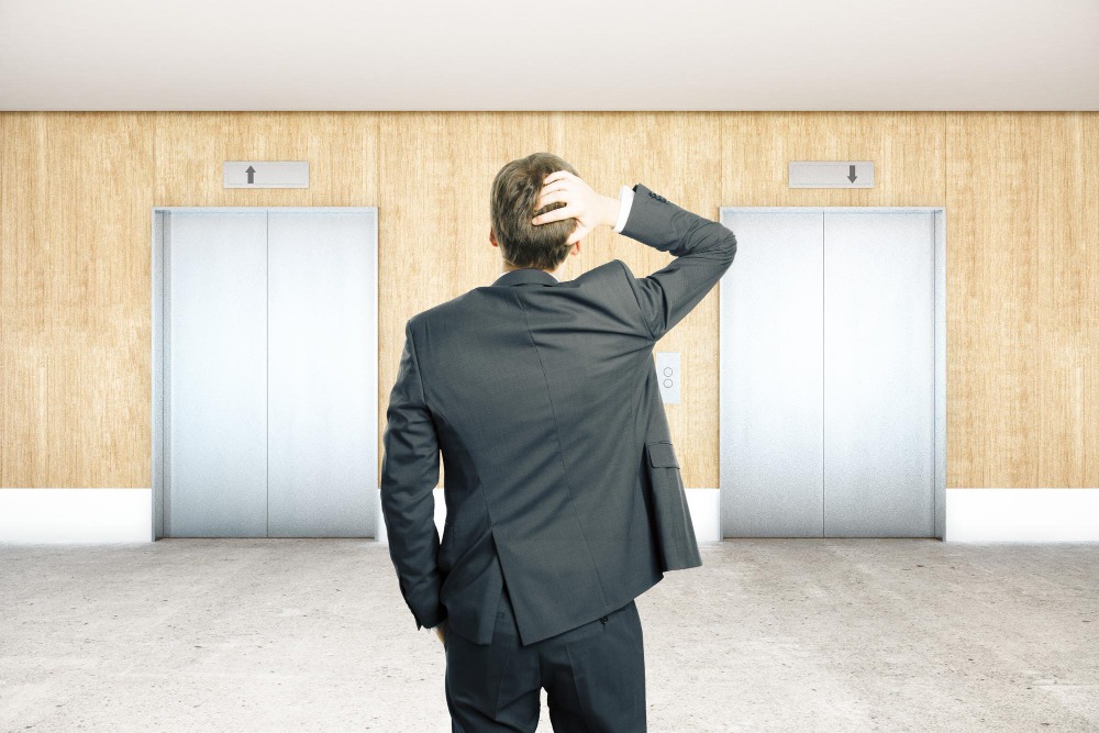 A man scratching his head in front of office lifts to show office asset management