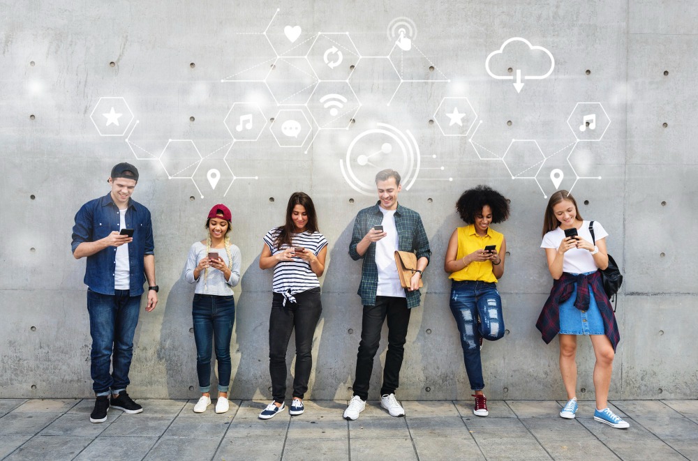 People with mixed ethnicity standing against a grey wall holding phones with tech symbols imposed on the wall to represent community management app