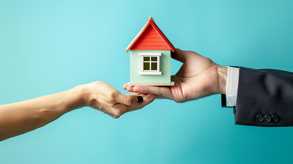 Image with one hand holding a home model with another hand underneath to show home handover